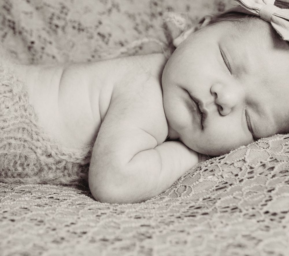 A peaceful newborn baby sleeping soundly on soft lace fabric in black and white photography.