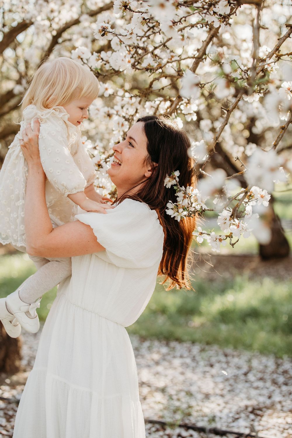 Sweet springtime moment in white dresses under blossoming cherry trees with soft golden sunlight filtering through.