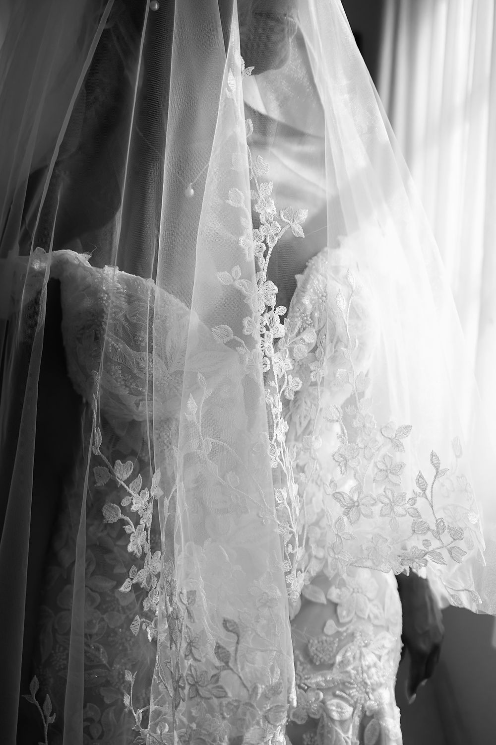 Close-up view of delicate lace and floral embroidery details on a white wedding veil in black and white.