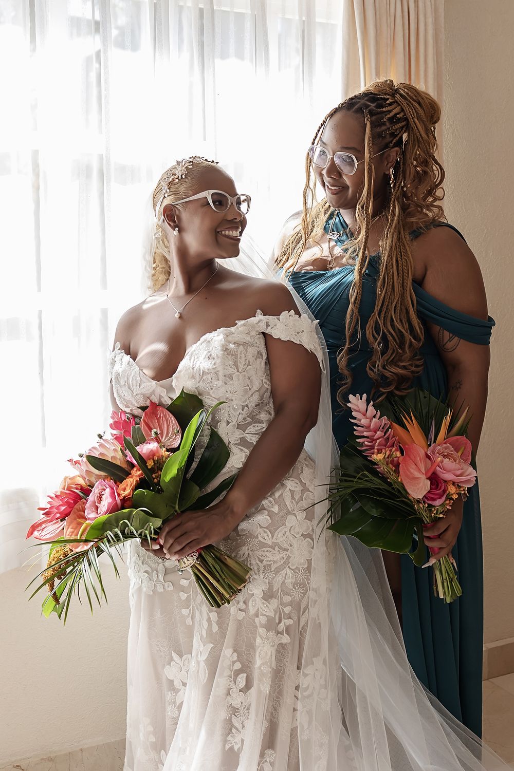 Bride standing in soft light by the window holding her bouquet.