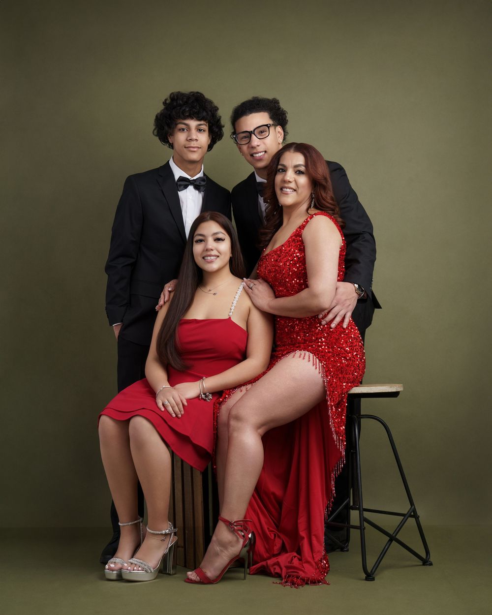 Four stylish figures in red and black formal attire pose together in a studio setting against a dark backdrop.