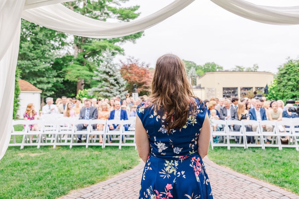 Outdoor wedding venue setup with white chairs in rows and a draped fabric canopy over a stone patio area.