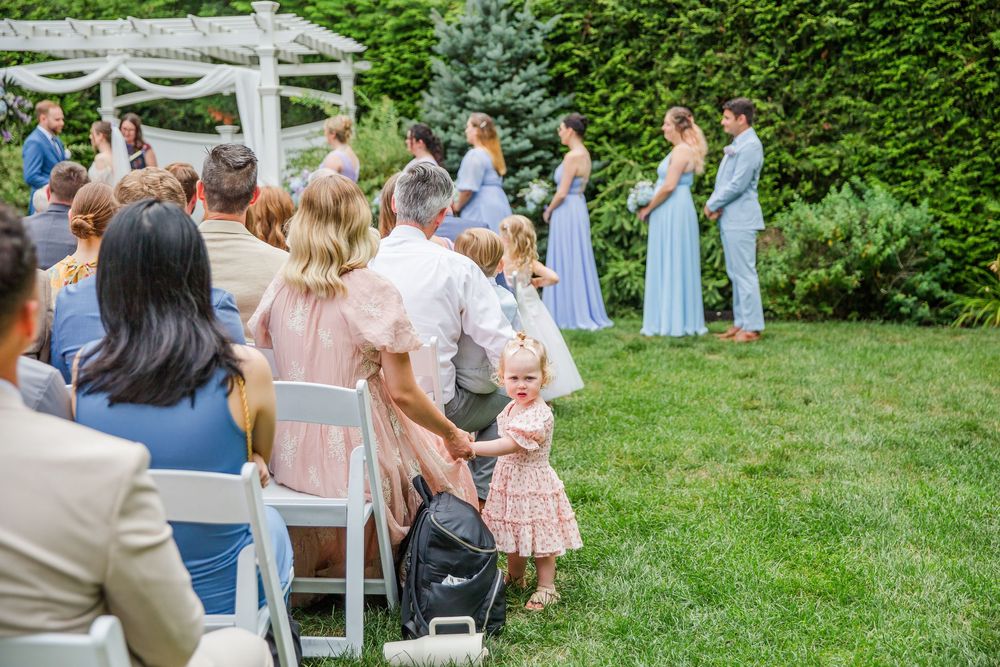 Wedding guests stand scattered across a lush green lawn during an outdoor summer ceremony.