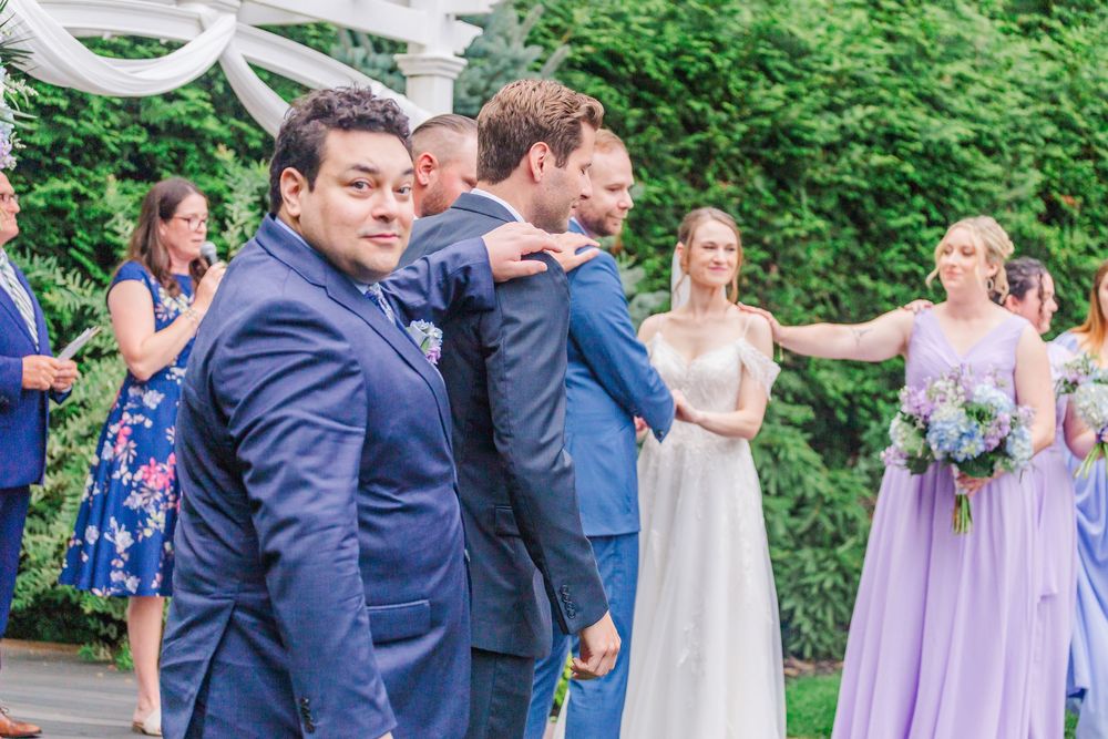 Joyful wedding party celebrating outdoors with guests in lavender dresses and navy suits.