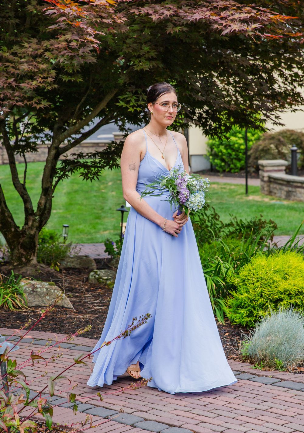 Light blue bridesmaid dress with flowing skirt and delicate bouquet under a blooming tree in garden setting.