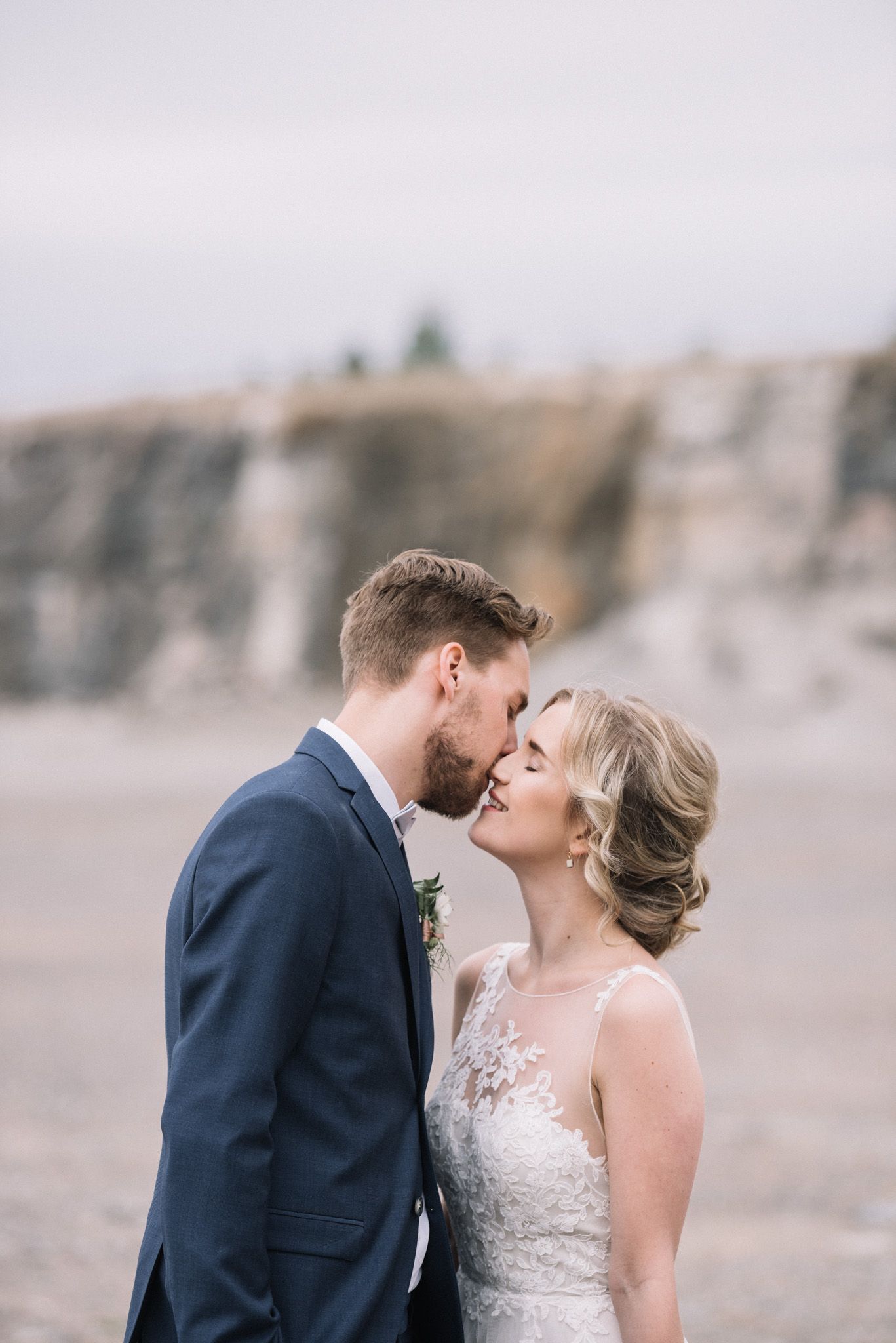 A romantic wedding portrait set against rugged cliffs with a couple sharing an intimate moment in elegant attire.