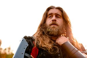 A person with long blonde hair and a beard looks upward during golden hour with sunlight illuminating their features.