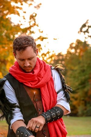 Medieval costume with red scarf and leather accessories against autumn foliage at golden hour sunset.