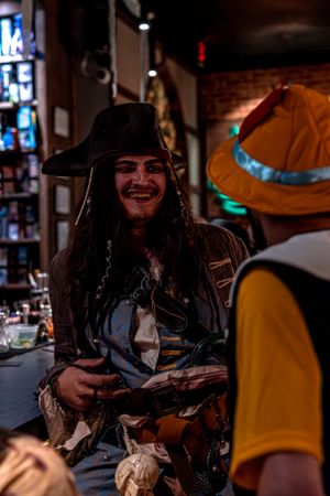 A costumed pirate interacts with another person wearing an orange hat in a dimly lit indoor setting.