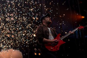 Guitarist on stage performs with red electric guitar while sparkling pyrotechnics create a dramatic backdrop during concert.