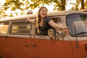 A rustic orange vintage Volkswagen van with a passenger looking joyfully out the window at sunset.