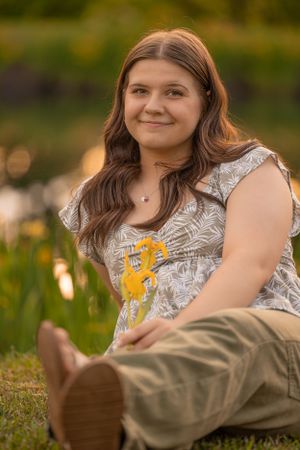Someone sits in a flowery field wearing a white patterned top and khaki pants during golden hour sunset.