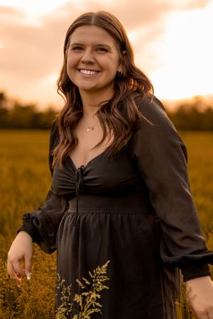 A joyful portrait in a golden field at sunset wearing a black dress with long-sleeved details.
