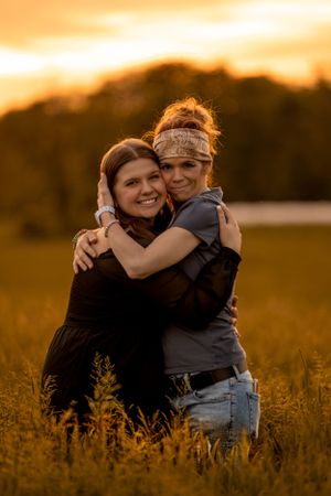 Two people embrace in a golden wheat field during sunset, creating a warm and intimate outdoor portrait.