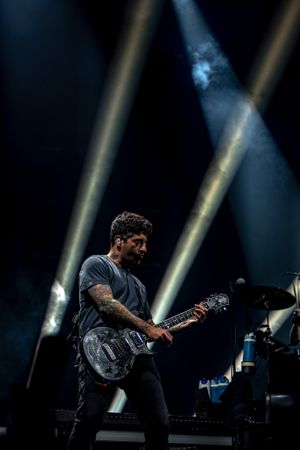 Musician playing electric guitar on dark stage with dramatic crossing spotlights beaming through smoke in background.