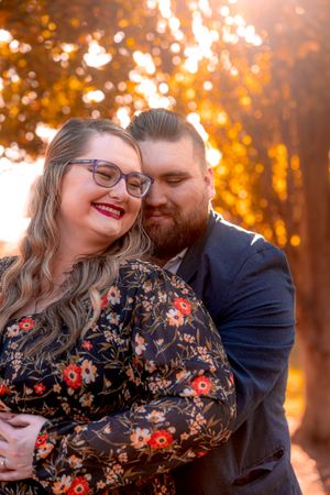 A couple embraces in front of golden autumn sunlight creating a warm romantic portrait setting.