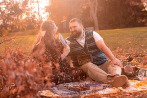 A couple enjoys an autumn picnic on a blanket surrounded by fallen leaves during golden hour sunset.