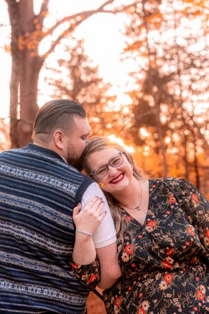 A romantic outdoor engagement photo showing tenderness between a couple during a warm autumn sunset.