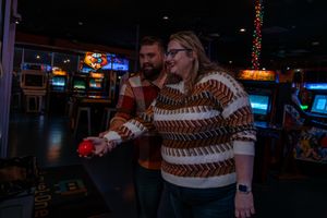 People singing together at a dimly lit karaoke bar wearing patterned sweaters.