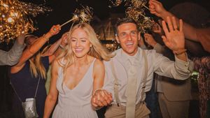A newlywed couple joyfully runs through a crowd of wedding guests holding sparklers during their evening reception celebration.
