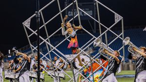 Marching band performers create dynamic formations with scaffolding and instruments during a nighttime stadium show.