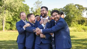 Groomsmen in navy blue suits sharing a celebratory moment outdoors on a sunny day.