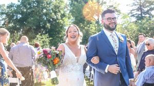 Joyful newlyweds smile and celebrate during an outdoor autumn wedding ceremony with colorful flowers.