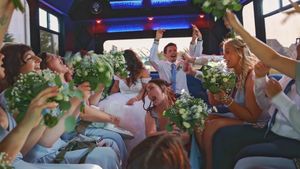 Celebration on a party bus with people raising green bouquets and laughing together in a festive atmosphere.