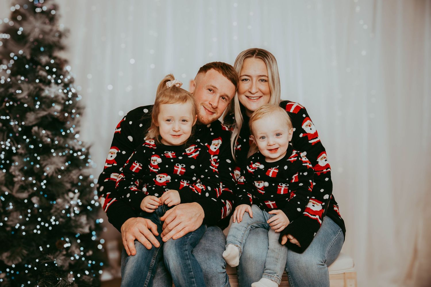 Family wearing matching floral Christmas sweaters pose by decorated tree.