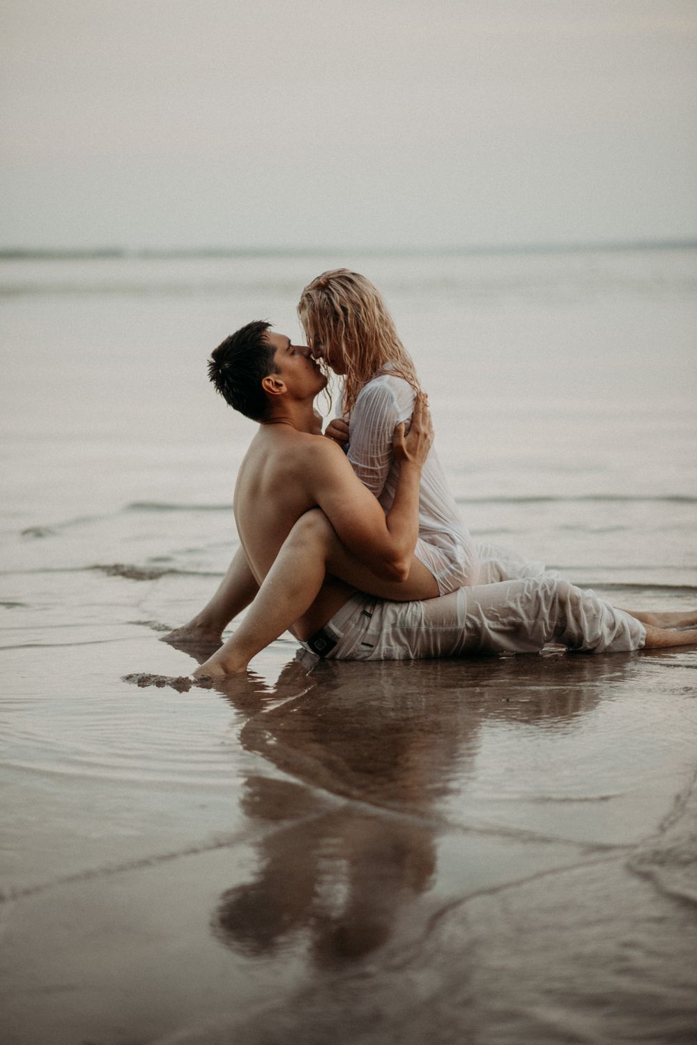 Romantic couple embracing in shallow water during sunset photoshoot.