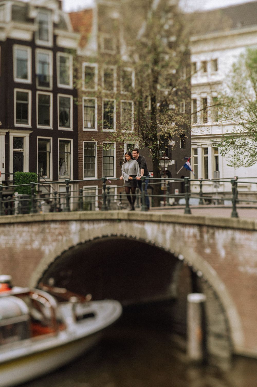 Romantic couple sharing a moment on a historic Amsterdam canal bridge with traditional Dutch architecture in background.