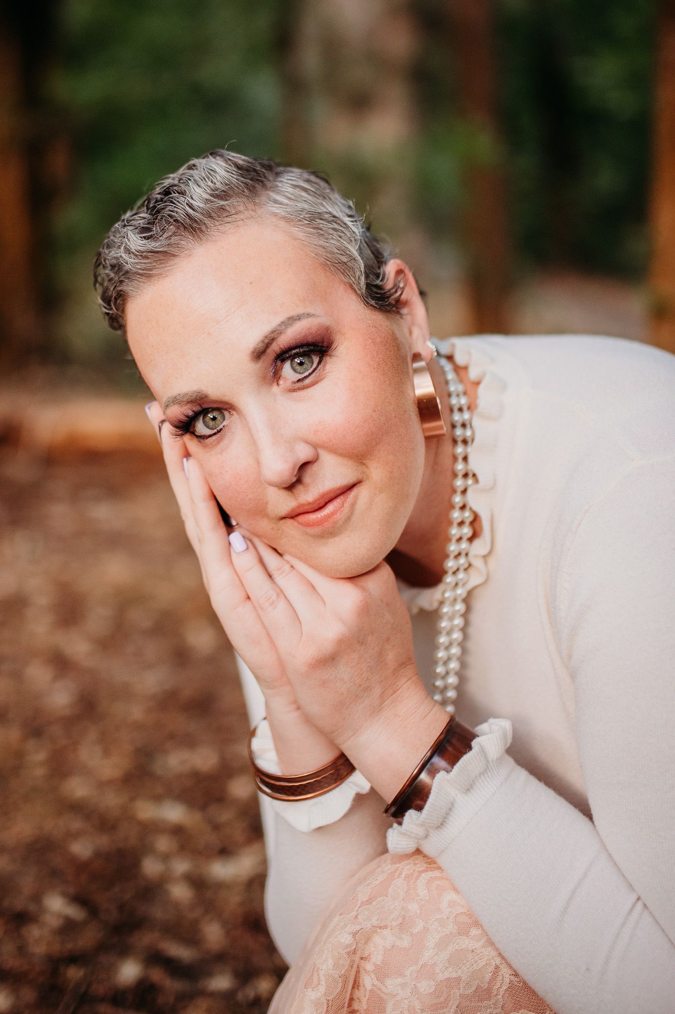 Elegant portrait with pearl necklace and cream sweater in forest setting.