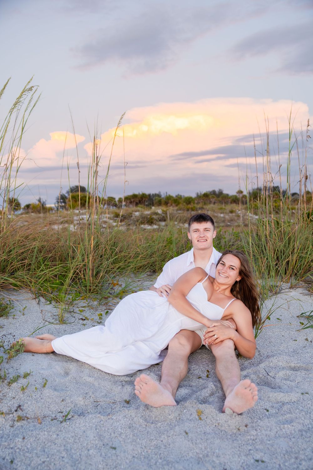 Romantic couple relaxing together on sandy beach dunes at golden sunset.