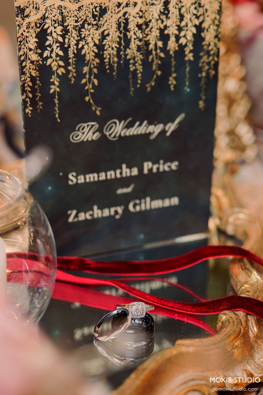 Wedding invitation with elegant calligraphy names and red ribbon detail against dark background with golden decor.