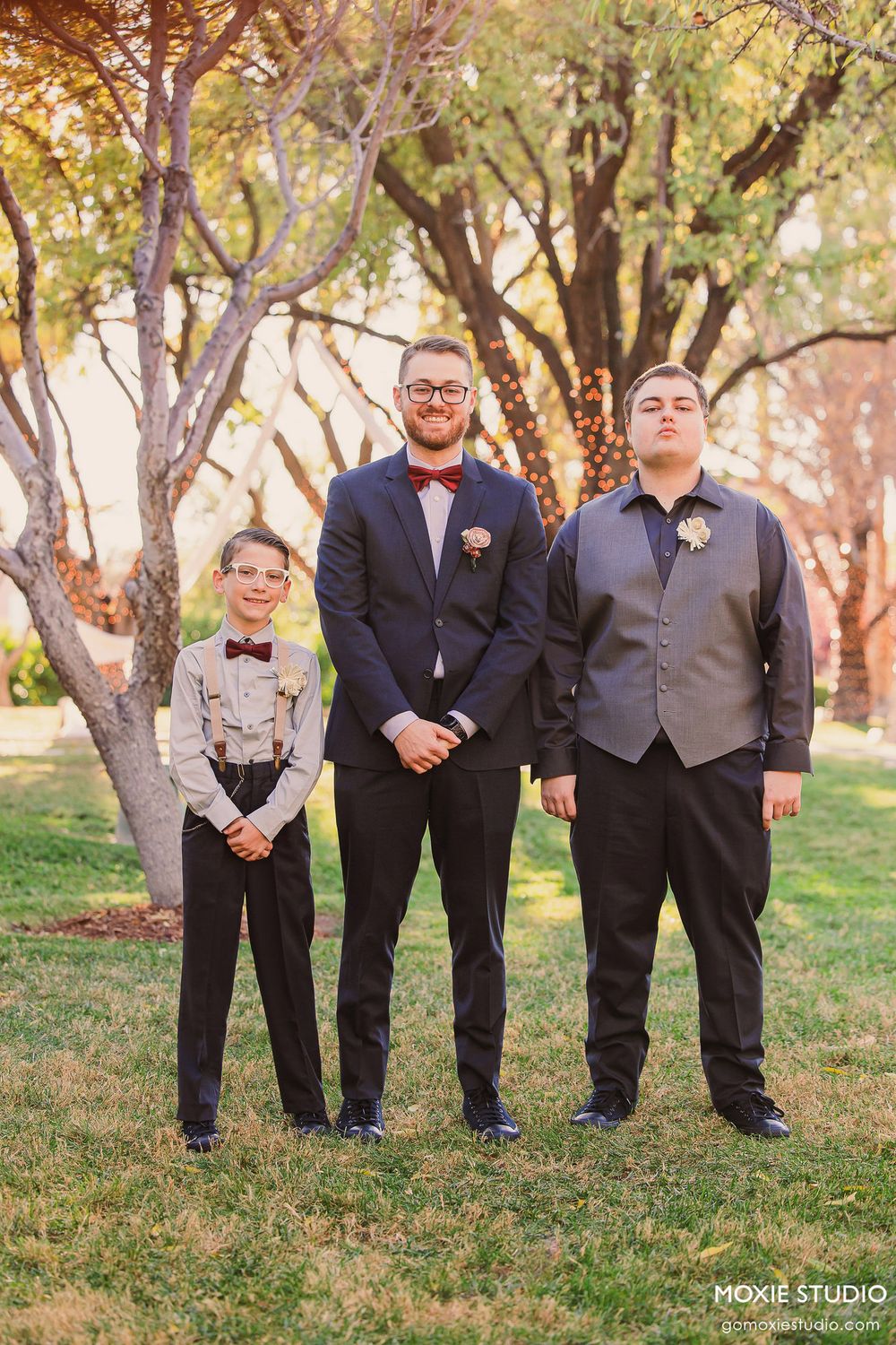 Groomsmen in navy suits and gray vests pose together on grass during outdoor wedding photoshoot.