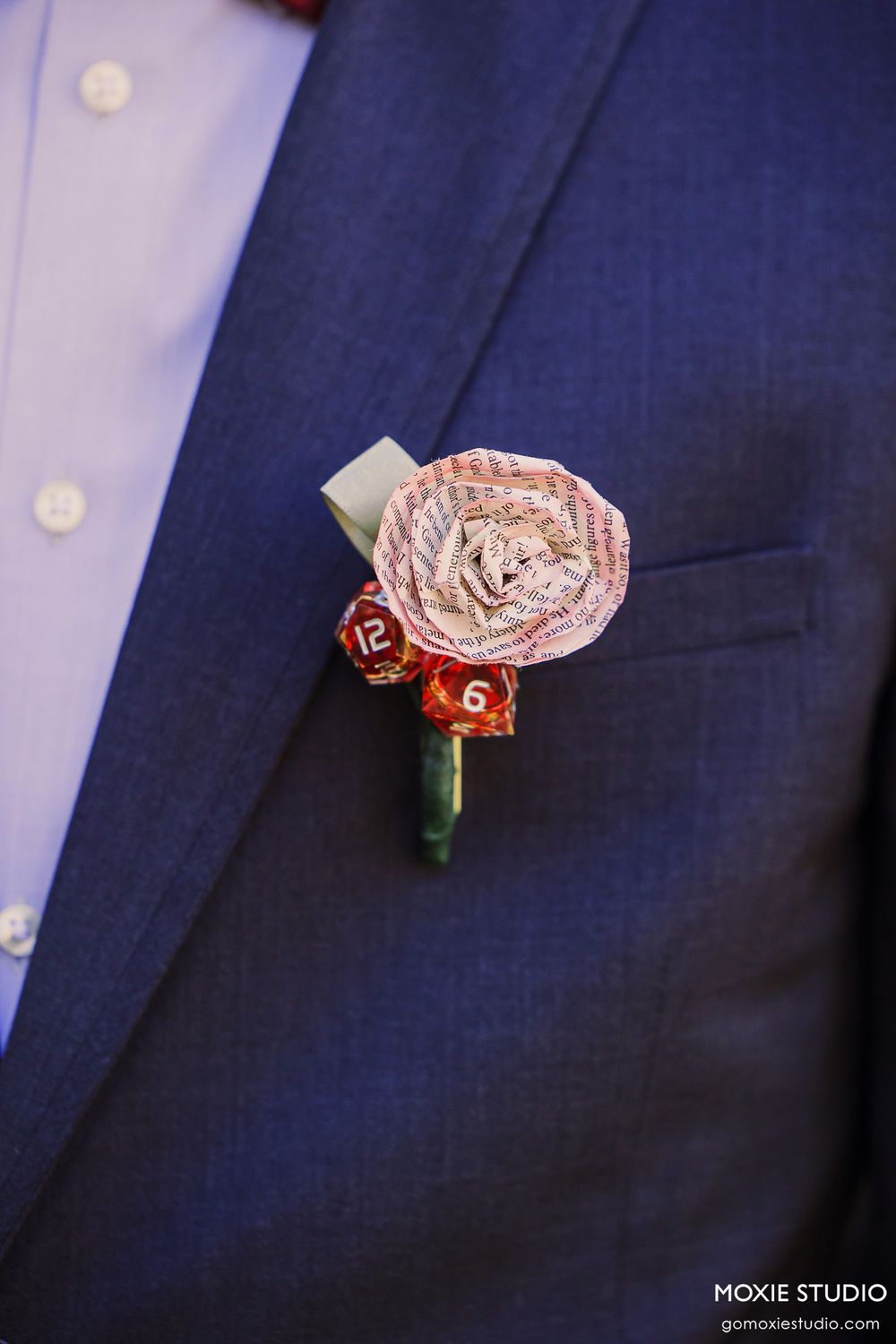 Close-up progression of a delicate pink fabric boutonniere being pinned to a navy blue suit jacket.