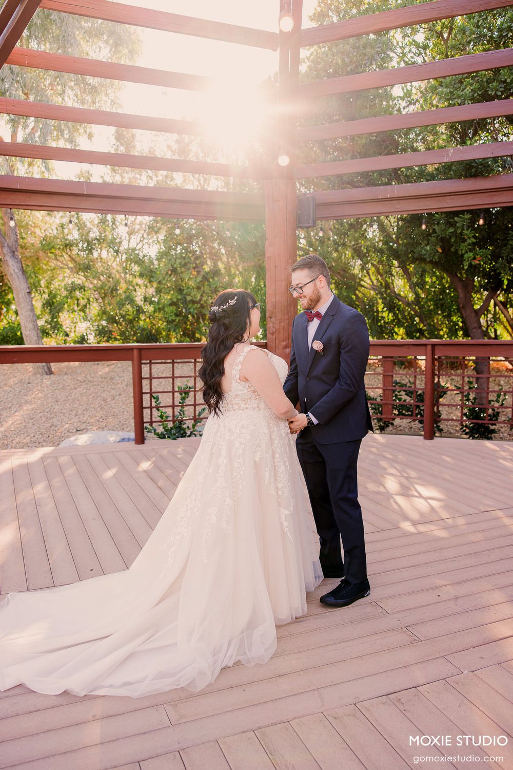 Romantic wedding couple shares intimate moments under wooden pergola during sunset photoshoot.