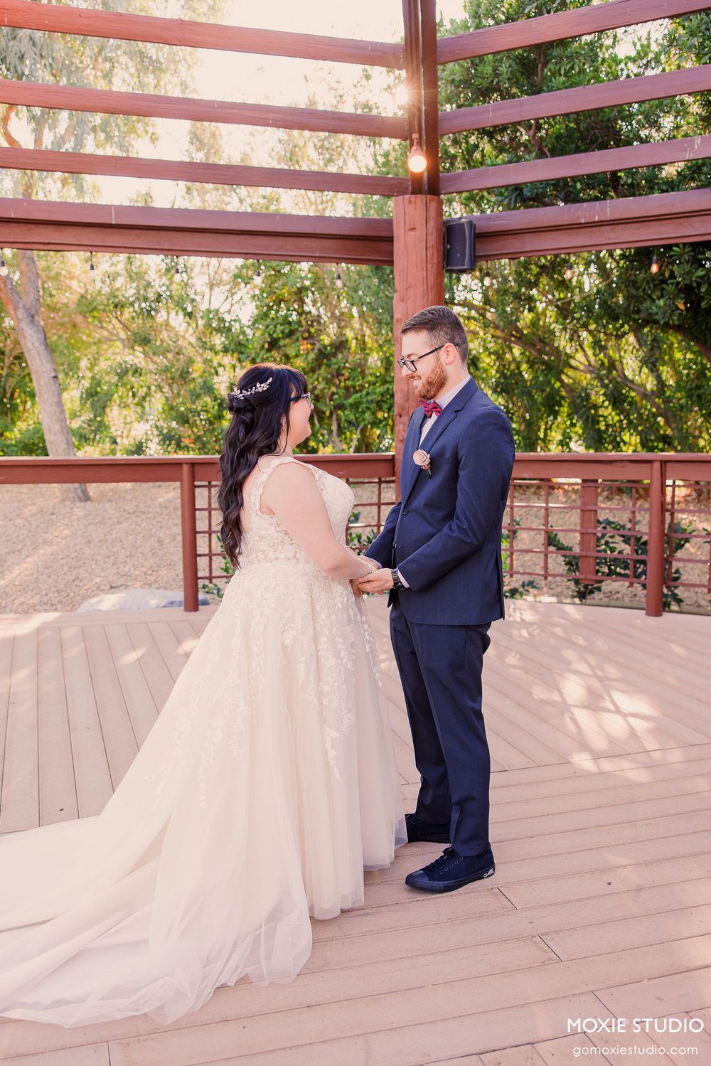 A wedding couple shares a romantic first look moment under a wooden pergola during their outdoor ceremony.