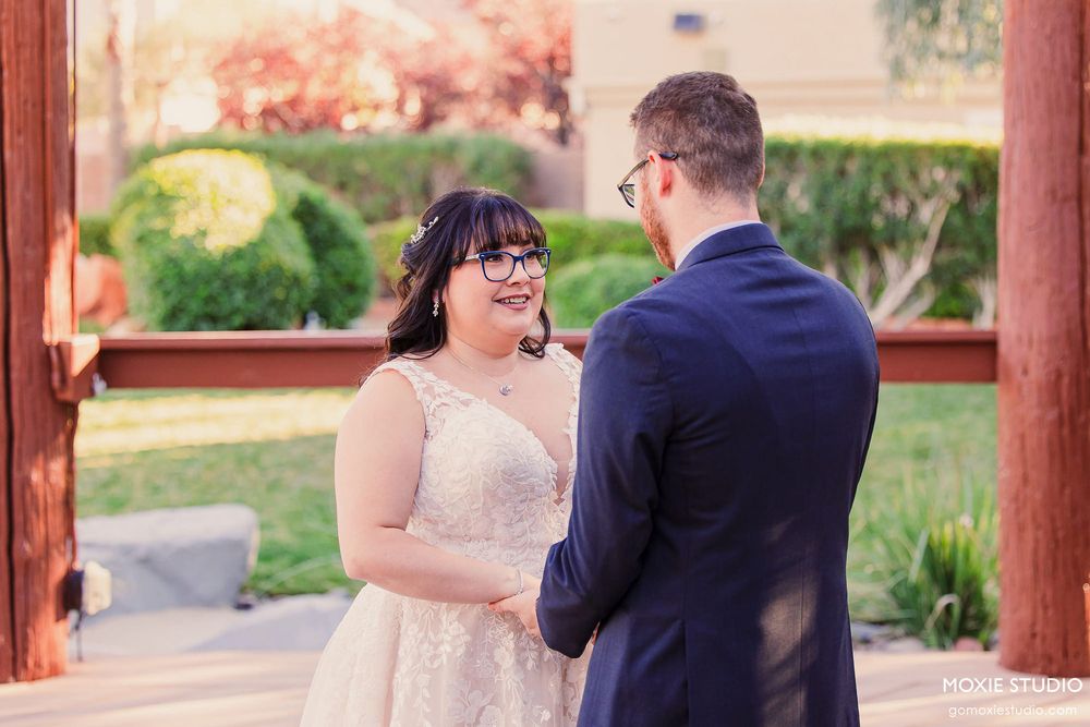 A couple shares an intimate moment under a rustic wooden pergola during their wedding ceremony.