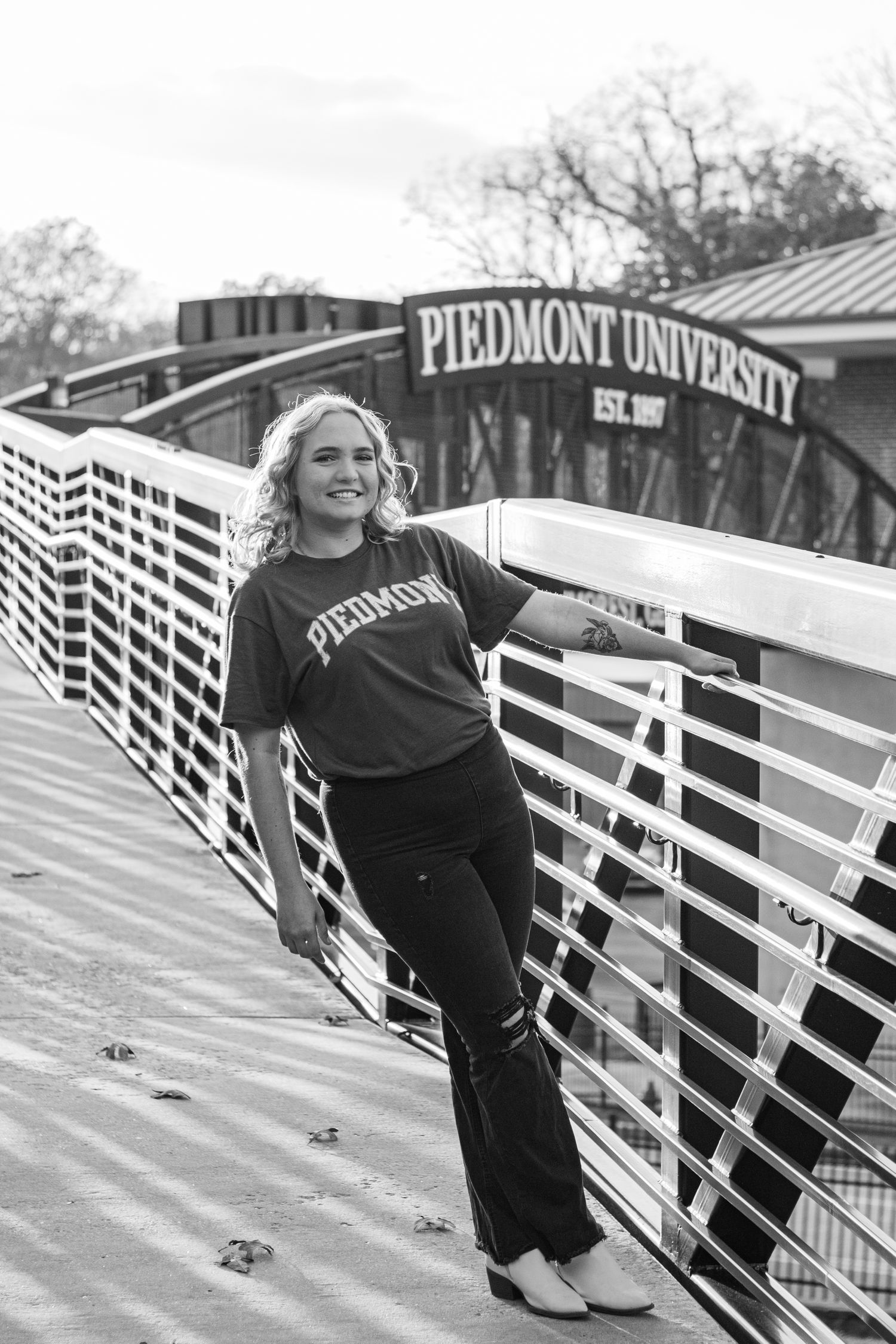 A student poses on a bridge with the Piedmont University sign visible in the background.