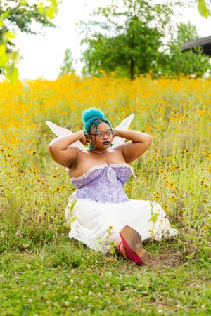 A person in a purple corset poses playfully in a field of yellow wildflowers.