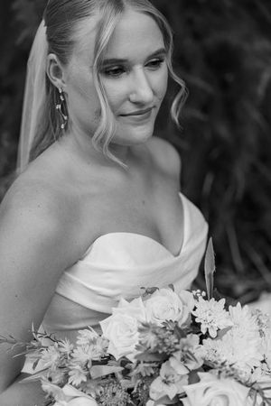 Black and white portrait of a bride in a strapless gown holding a floral bouquet, wearing a veil and elegant earrings.