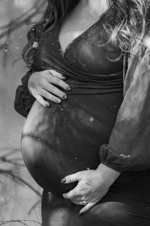 Black and white maternity photo showing pregnant belly with hands gently cradling the bump in artistic silhouette.
