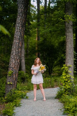 Whimsical forest path portrait with white dress and sunflower bouquet.
