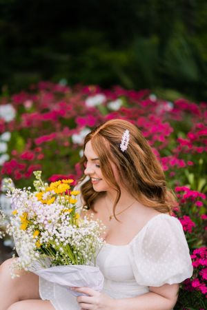 Dreamy garden portrait with wildflower bouquet and white puff sleeve dress among pink blooms.