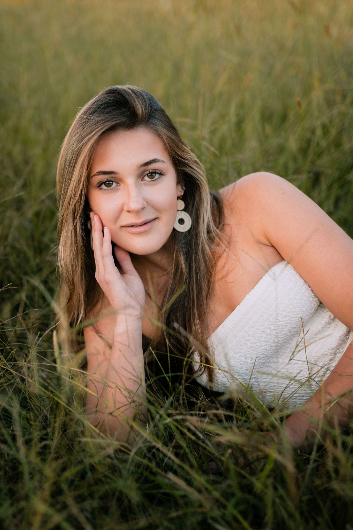 A portrait of a woman in white lying in tall grass during golden hour.