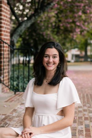 A portrait of someone in a white dress sitting on brick steps during spring.