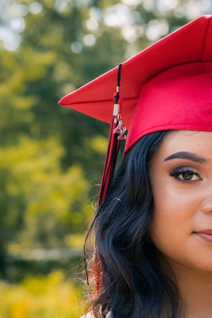 Close-up portrait of a graduate wearing a red cap with tassel against a blurred natural background.