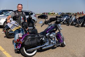 A motorcyclist stands next to a purple Harley-Davidson motorcycle in a parking lot.