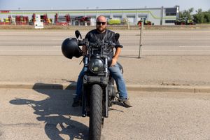 A biker sits on a black motorcycle in an open parking lot on a sunny day.